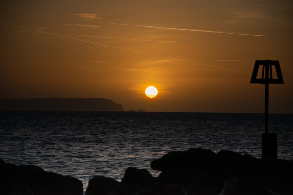 the sun is setting over the ocean with rocks in the foreground