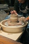 Artisan at work shaping a clay vase on a pottery wheel in a sunlit studio.