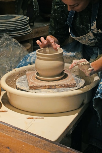 A woman artistically shaping a ceramic vase.