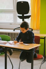 a young boy sitting at a desk writing on a piece of paper