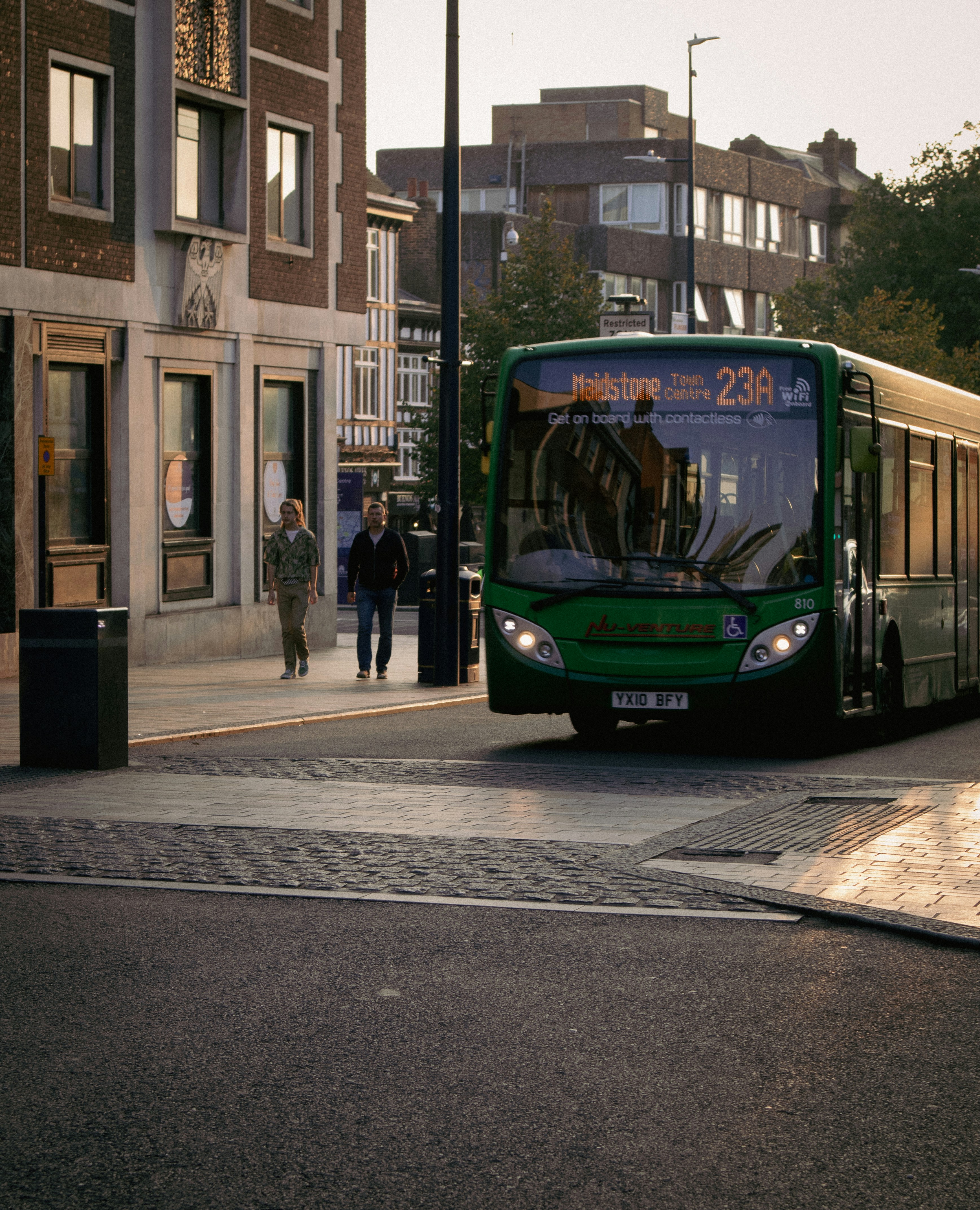 a green bus driving down a street next to tall buildings