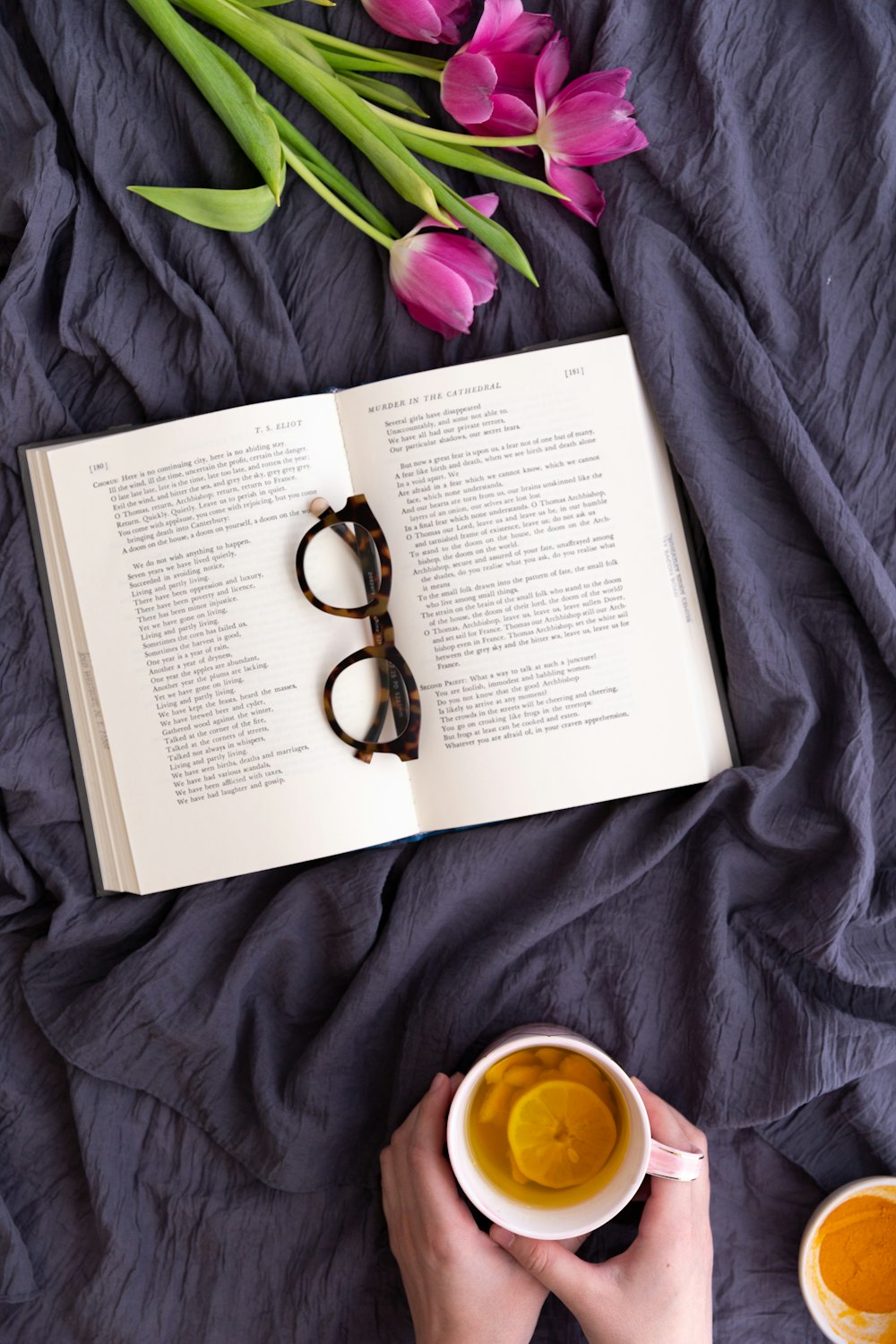 a person is reading a book and drinking a cup of tea