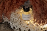 A glass bottle of perfume labeled 'Bal D'Afrique' by Byredo is surrounded by shredded paper and decorative dried grasses. The scene is softly lit, creating a warm and inviting ambiance.