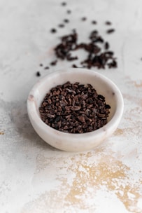 A jar of dark cacao seed butter on a slate slab, with raw cacao nibs and seeds scattered around in warm light.