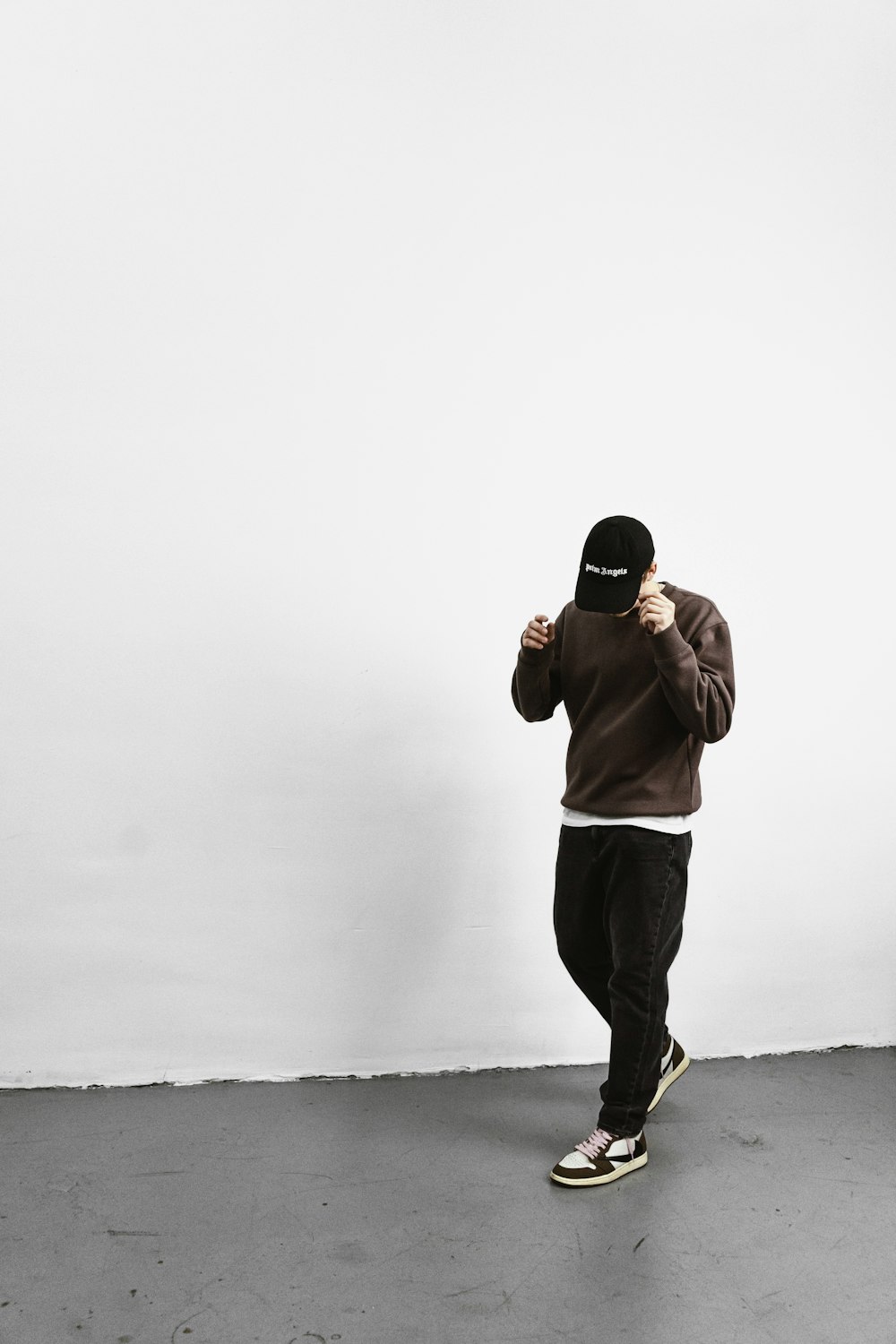a man in a brown hoodie is standing in front of a white wall