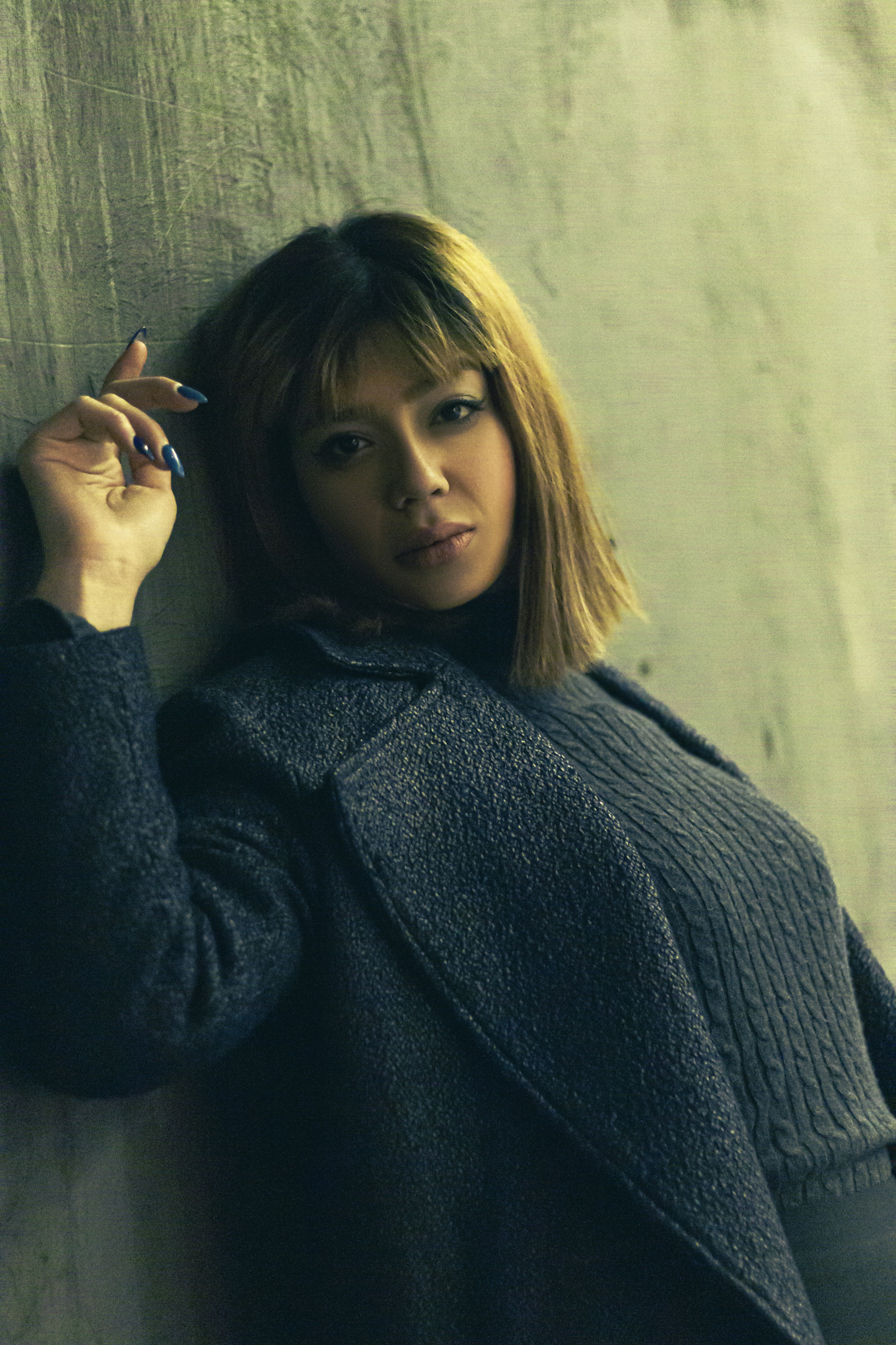 a woman leaning against a wall with a cigarette in her hand