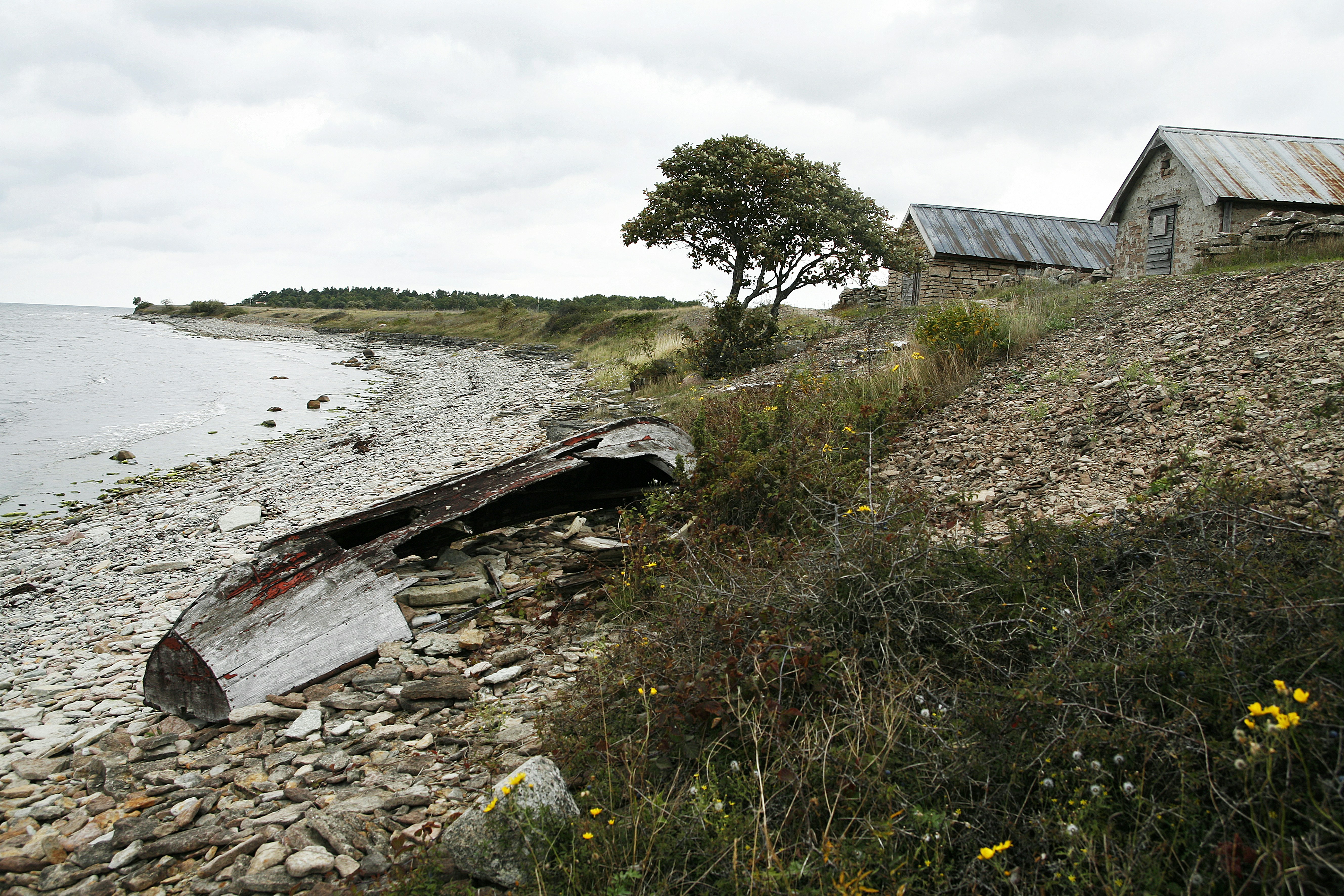 An old boat sitting on a rocky shore next to a body of water photo ...