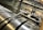 A close-up view of industrial machinery, featuring metallic cylindrical rollers and mechanical components interconnected with pipes and wires. The perspective highlights the mechanical complexity and precision engineering.