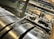 A close-up view of industrial machinery, featuring metallic cylindrical rollers and mechanical components interconnected with pipes and wires. The perspective highlights the mechanical complexity and precision engineering.