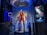A high-tech suit displayed in a futuristic setting, illuminated by focused lighting. The surroundings include digital screens showing technical data and designs related to the suit. The environment appears to be a lab or exhibit with metallic and technological elements.