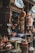 A shop displaying a variety of hanging and shelved copper kitchenware. The display includes pots, pans, and kettles with a man positioned next to the shelves. The scene showcases a traditional market atmosphere.
