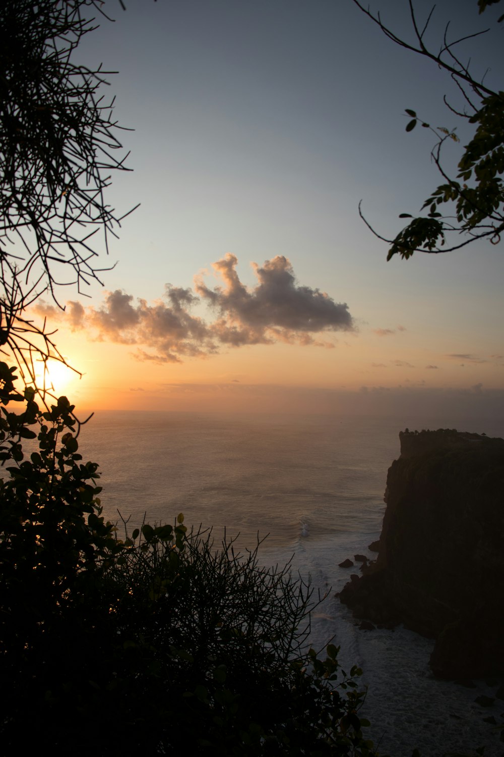 the sun is setting over the ocean from a cliff