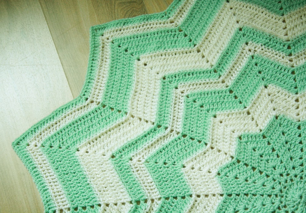 um cobertor de crochê verde e branco em um piso de madeira