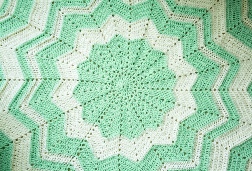 a green and white crocheted blanket on a bed