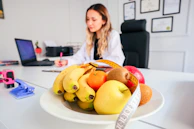 a woman sitting at a desk with a bowl of fruit