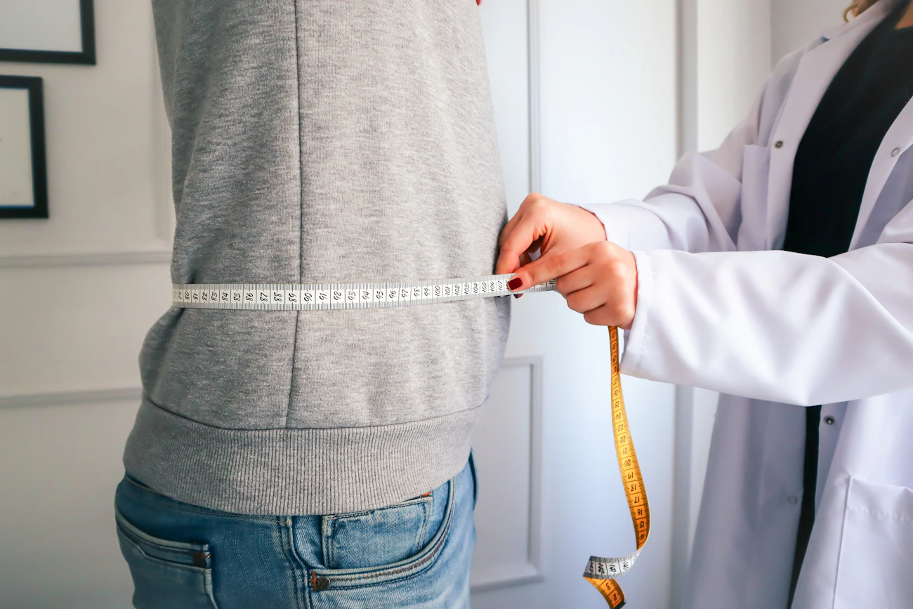 Close-up of a woman measuring her waist with a measuring tape, representing the body-contouring focus of ONDA treatment across the abdomen, waist, arms and thighs