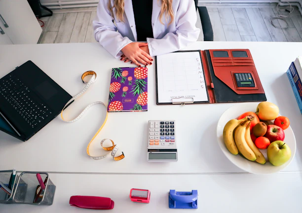 a woman sitting at a table with a plate of fruit and a calculator