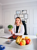 a woman sitting at a desk holding a piece of broccoli