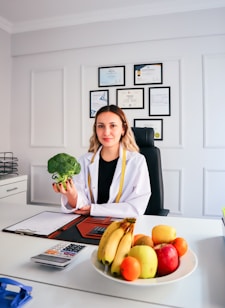 a woman sitting at a desk holding a piece of broccoli