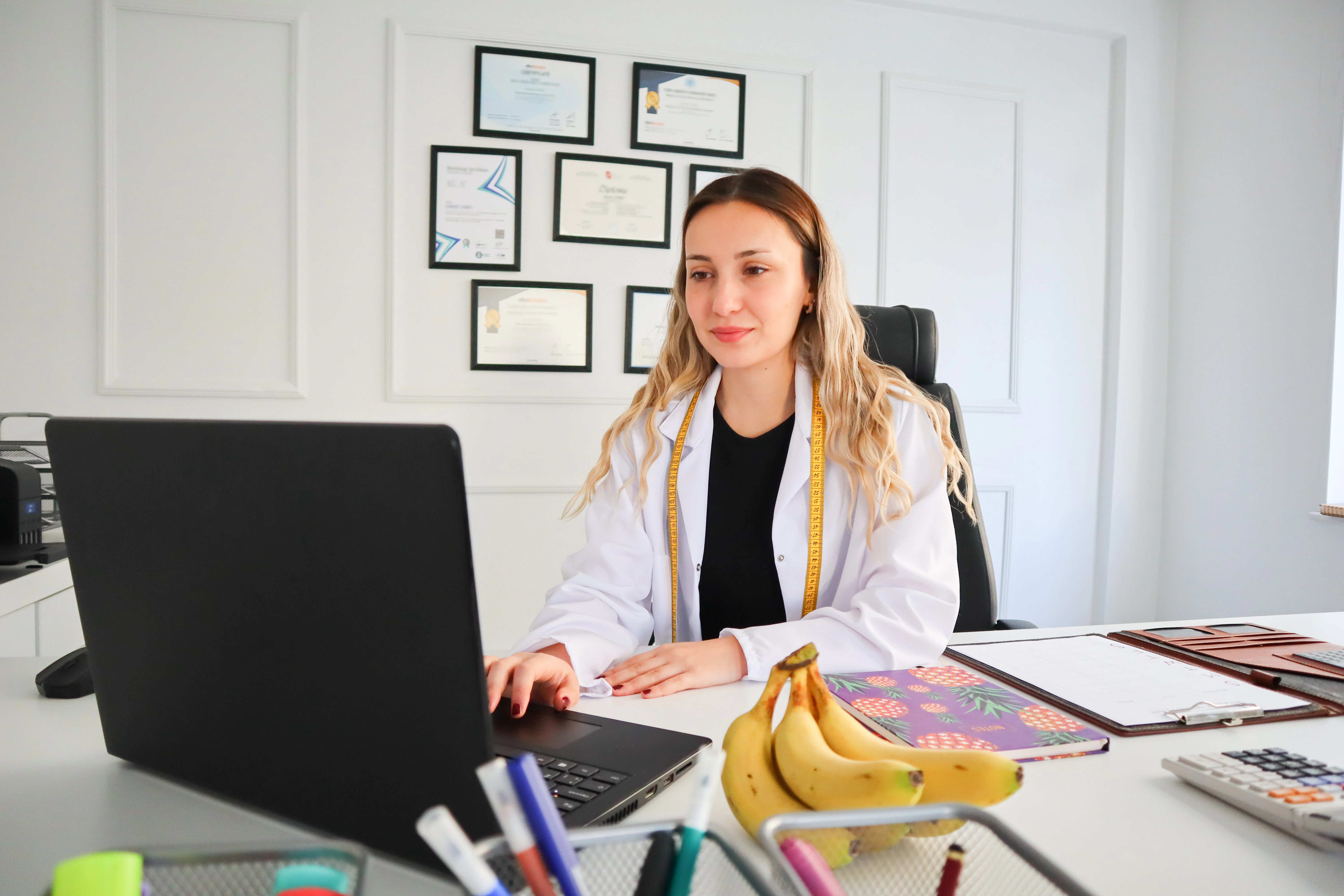 a woman sitting at a desk with a laptop and a bunch of bananas