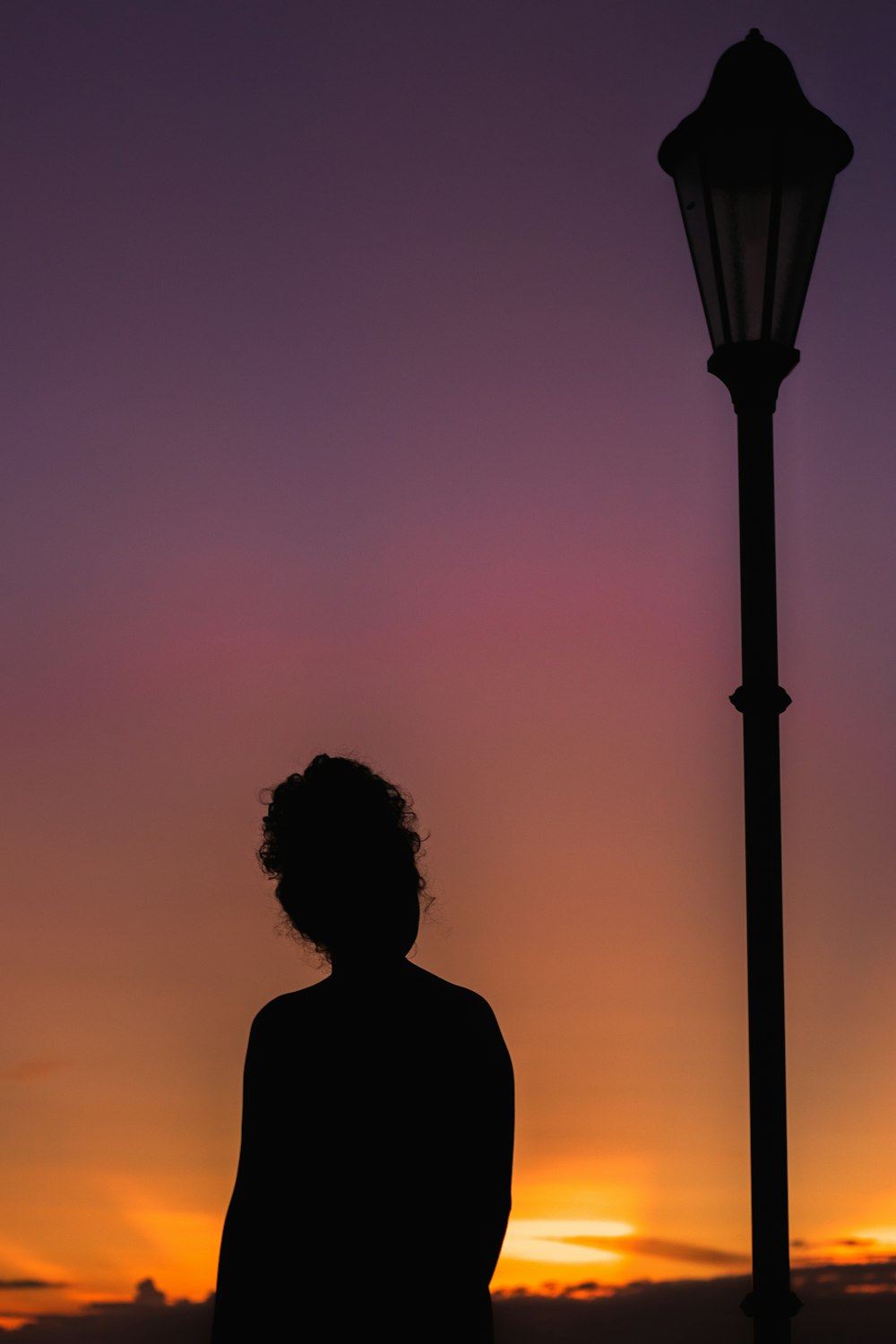 a woman standing next to a street light at sunset