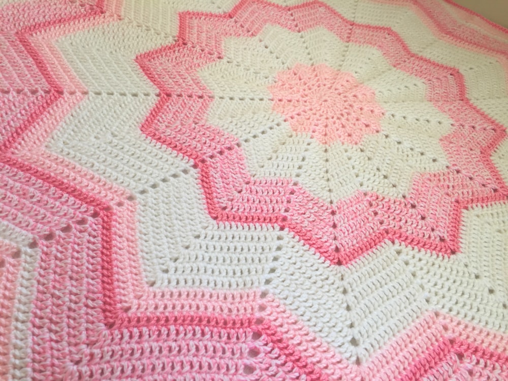 a pink and white crocheted blanket on a bed