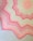 A crocheted blanket featuring a zigzag pattern with alternating shades of pink and cream. The design includes starburst motifs and textured stitching, creating a visually appealing contrast.