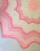 A crocheted blanket featuring a zigzag pattern with alternating shades of pink and cream. The design includes starburst motifs and textured stitching, creating a visually appealing contrast.
