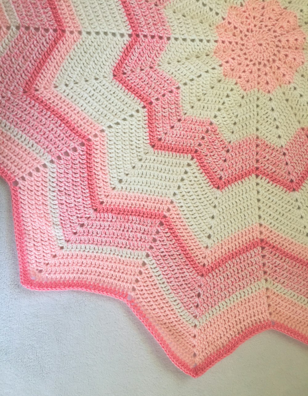 a pink and white crocheted blanket on a bed