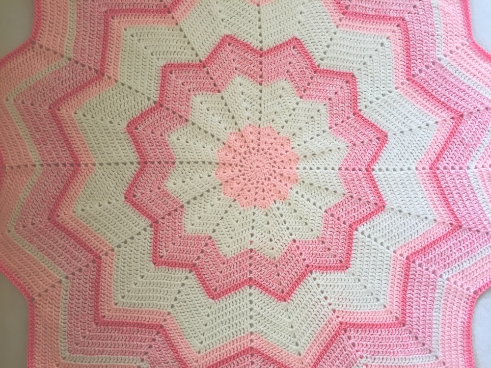 a pink and white crocheted blanket on a table