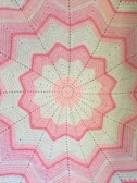a pink and white crocheted blanket on a bed
