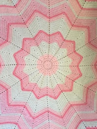 a pink and white crocheted blanket on a bed
