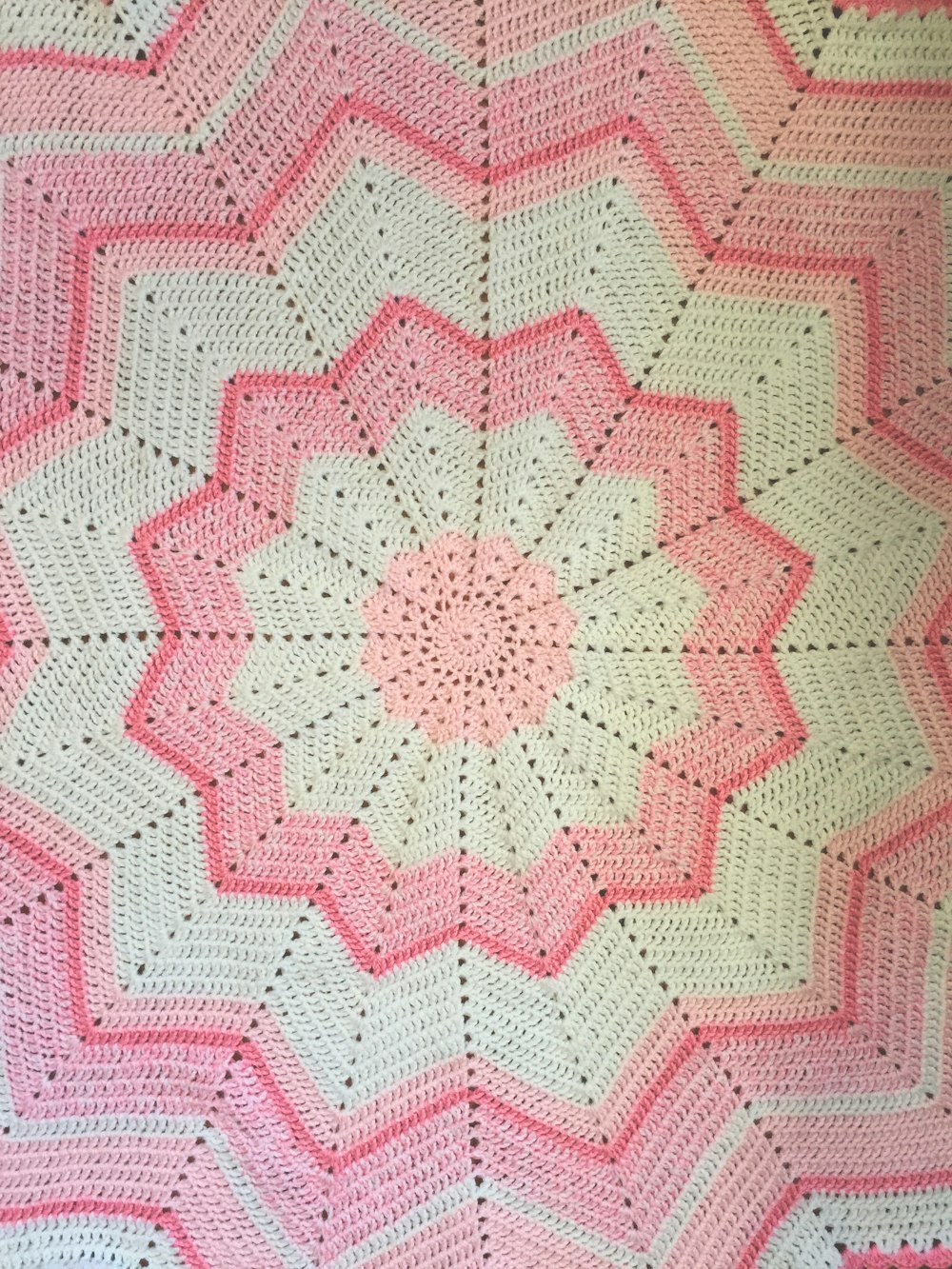 a pink and white crocheted blanket on a bed