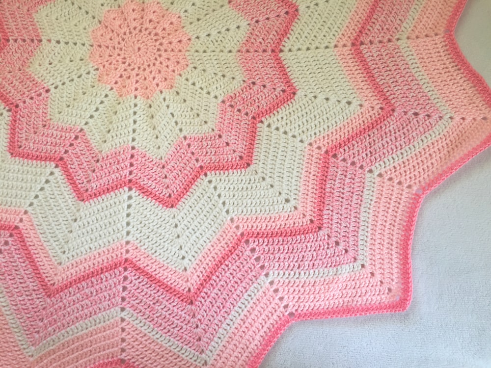 a pink and white crocheted blanket on a bed