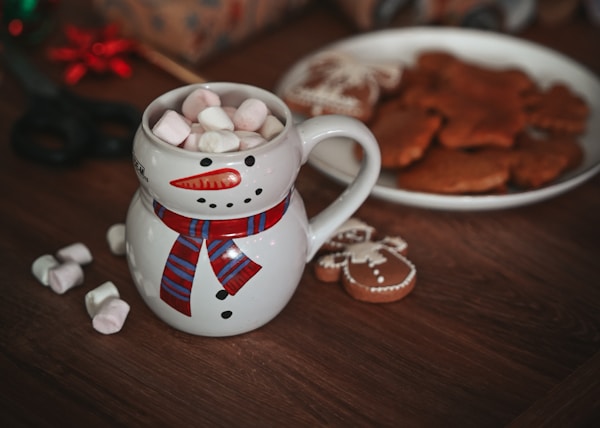 a mug with marshmallows in it next to a plate of cookies