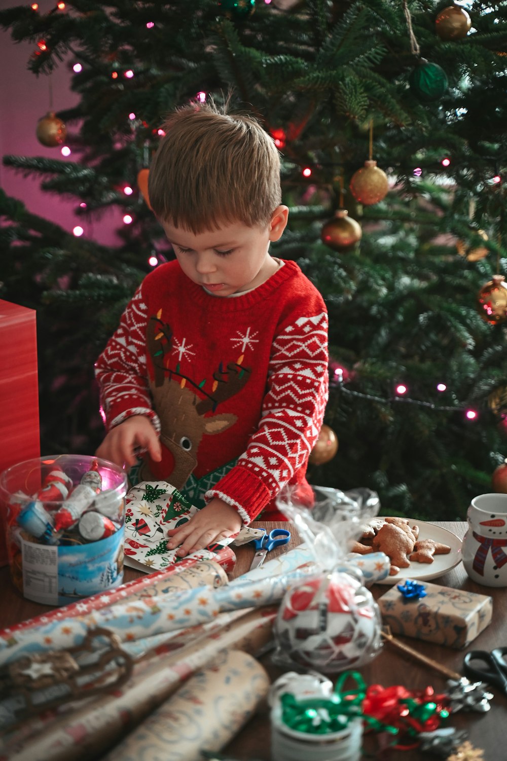 a young boy in a red sweater is decorating a christmas tree