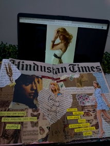 A laptop displaying a webpage with an image of a woman with blonde hair is visible in the background. In the foreground, there is a creative collage on the page of a Hindustan Times newspaper. The collage includes various cut-out images and text fragments. There are images of a woman, flowers, and handwritten notes with phrases like 'forever and always,' 'when you are young they assume you know nothing,' and 'she's an old soul with young eyes, a vintage heart, and a beautiful mind.' Dried wheat stalks and decorative elements are also part of the collage.