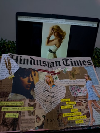 A laptop displaying a webpage with an image of a woman with blonde hair is visible in the background. In the foreground, there is a creative collage on the page of a Hindustan Times newspaper. The collage includes various cut-out images and text fragments. There are images of a woman, flowers, and handwritten notes with phrases like 'forever and always,' 'when you are young they assume you know nothing,' and 'she's an old soul with young eyes, a vintage heart, and a beautiful mind.' Dried wheat stalks and decorative elements are also part of the collage.