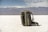 A backpack is placed on an expansive white salt flat with a mountain range in the background. The sky is partly cloudy, adding depth to the landscape. The backpack is equipped with a carabiner and other gear, suggesting a readiness for adventure or travel.