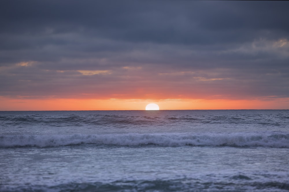 the sun is setting over the ocean with waves