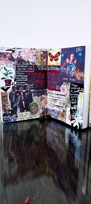 A creative and colorful journal spread filled with various cutouts, stickers, and notes. It features references to a popular TV show with images of characters, symbols, and quotes. The layout is busy, vibrant, and visually engaging, combining elements of collage art and scrapbook design.