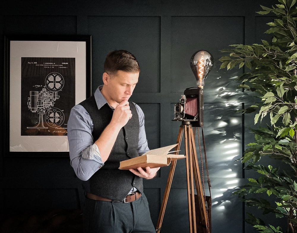 a man looking through a book while standing next to a tripod