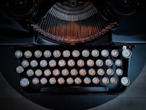 A vintage typewriter with round keys and metallic accents, displaying an intricate mechanical design. The keys are arranged in a classic QWERTY layout, and the dark frame contrasts with the softly lit keys.