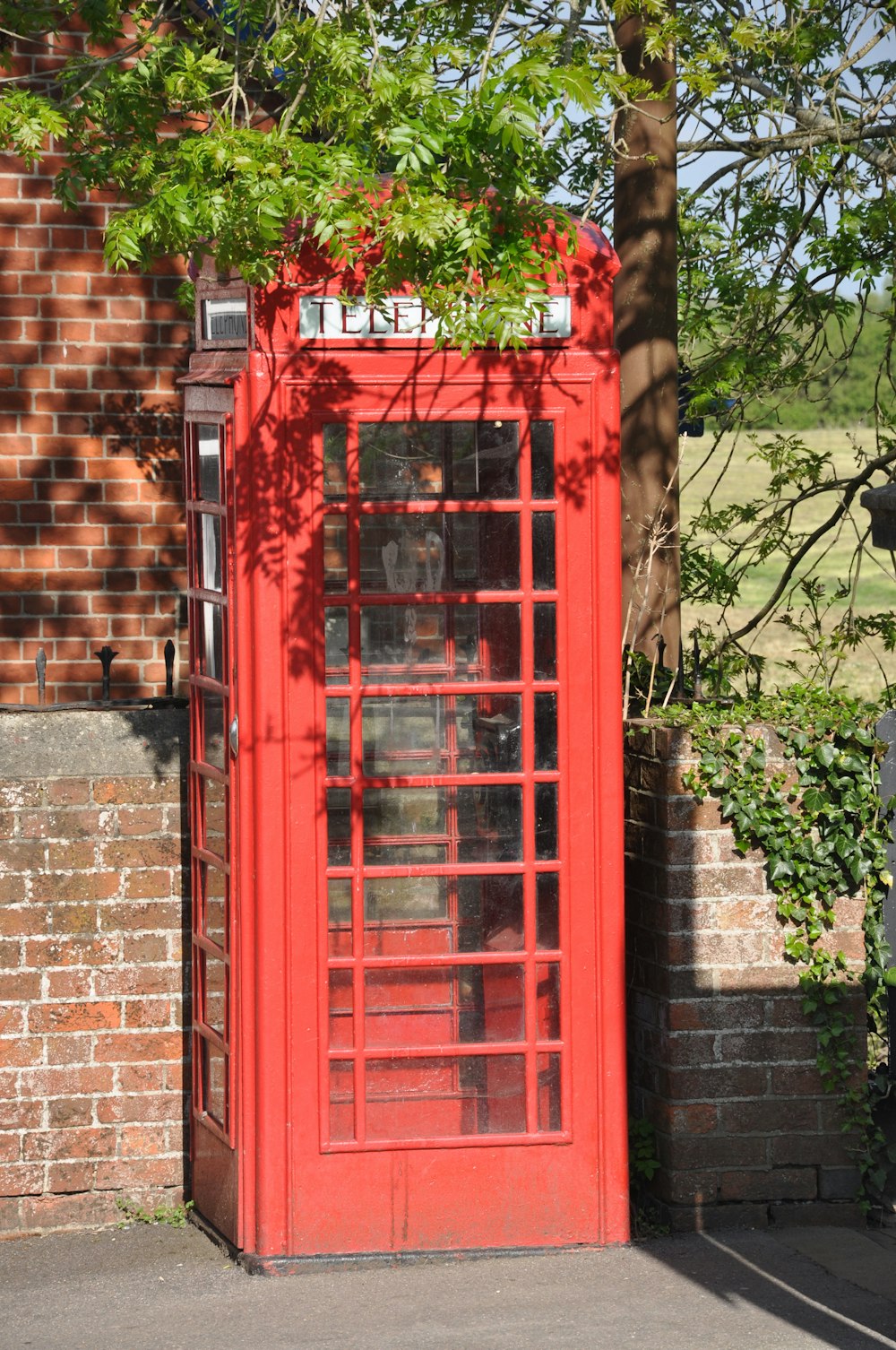 a red phone booth sitting next to a tree