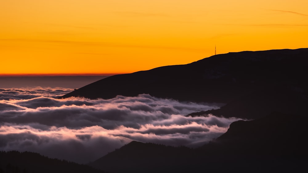 the sun is setting over the clouds in the mountains