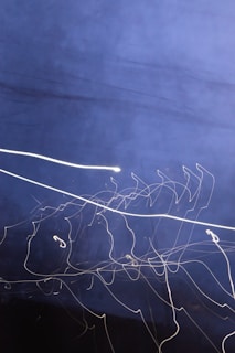 A dark blue background with streaks of white light forming abstract, swirling patterns. The dynamic lines appear to be created through long exposure photography, giving a sense of motion and fluidity.