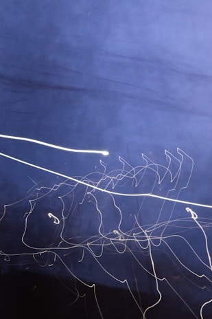 A dark blue background with streaks of white light forming abstract, swirling patterns. The dynamic lines appear to be created through long exposure photography, giving a sense of motion and fluidity.