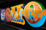 Close-up of a vibrant neon graffiti mural glowing against a dark wall.