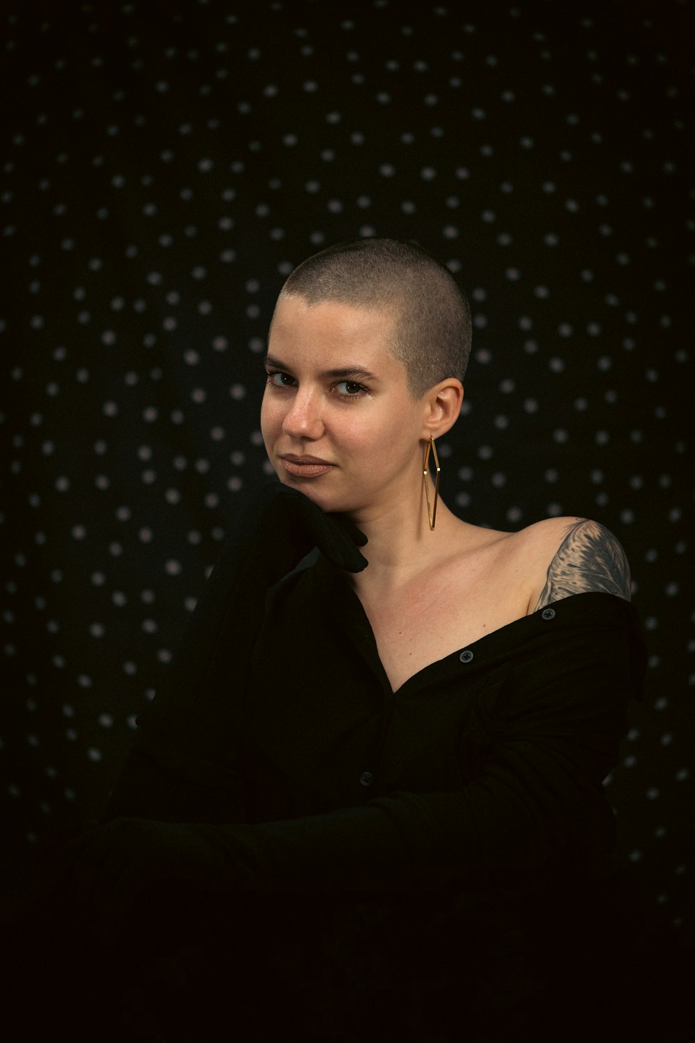 a woman with a shaved head standing in front of a black background