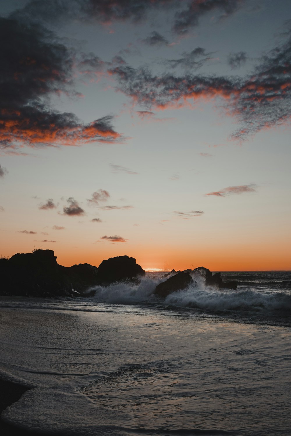 the sun is setting over the ocean and rocks